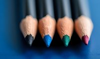 Macro view of colored pencil tips in black, blue, green, and pink arranged in row on blue background for art and creativity concepts.