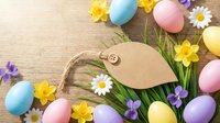 Colorful Easter eggs with spring flowers and blank kraft paper tag on wooden background. Festive holiday decoration for greeting cards and seasonal designs.