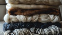 Neatly stacked skeins of natural wool yarn in white, brown and navy blue colors showing texture and softness of knitting materials for craft projects.