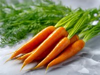 Fresh organic carrots with green tops lying on light background, macro food photography showing vibrant orange color and natural texture.