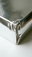 Shiny metallic silver foil wrapping paper corner with creased edges and reflective surface for gift packaging and holiday decorations.