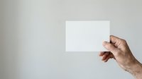 Caucasian male hand holding blank white card or paper against neutral gray background for mockup and branding purposes.