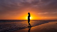 Silhouetted female jogger running along sandy beach at golden sunset, waves crashing, perfect for fitness, wellness, and lifestyle content.