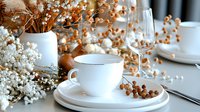 Elegant white porcelain teacup and saucer on table with dried baby's breath flowers in vase, wine glass and rustic autumn decorative elements creating cozy atmosphere.