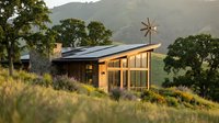 Modern eco-friendly house with solar panels and large windows nestled in rolling hills at sunset, sustainable architecture design for green living.