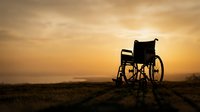 Empty wheelchair silhouetted against golden sunset sky on barren landscape, symbolizing hope, resilience, and overcoming challenges in healthcare and disability awareness contexts.