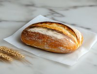 Fresh baked artisan bread loaf with crispy golden crust dusted with flour on white paper, marble surface with wheat stalks, food photography.