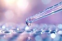 Macro shot of crystal clear water drop falling from glass pipette onto reflective surface with soft pink and purple bokeh background, showing surface tension.