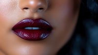 Close up of sensual dark burgundy glossy lips on smooth skin, showing professional makeup application and beauty details in soft lighting for cosmetic and fashion use.