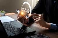 Professional businessman holding glowing non-stop support icon above laptop keyboard in modern office environment for customer service concepts.