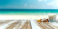 Amber medicine pills scattered on wooden deck with glass of water against blurred tropical beach and turquoise ocean background. Healthcare concept.