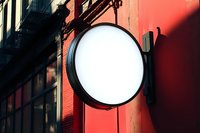 Blank circular storefront sign mounted on vibrant red building facade with urban architecture in background during sunset light.