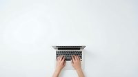 Hands typing on laptop computer from above on clean white background for business and technology concepts.