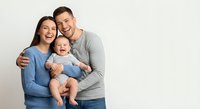 Happy young Caucasian family with baby boy laughing together in studio portrait on neutral background for parenting and lifestyle concepts.