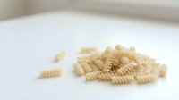 Whole wheat spiral pasta scattered on white surface, isolated ingredient for cooking and food preparation.