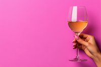 Female hand holding glass of rose wine against vibrant pink background, minimal composition with copy space for wine tasting events and celebrations.