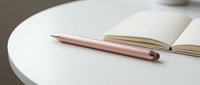 Open notebook with blank pages and rose gold stylus pen on white round table, suitable for writing, planning, education, and creative projects.