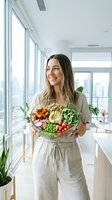 Young woman with long dark hair and East Asian ethnicity holding a colorful vegetable bowl in a bright modern kitchen with city views. Nutritionist or wellness professional promoting healthy eating and balanced diet lifestyle.