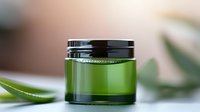 Green glass cosmetic jar with black lid on blurred natural background with aloe vera leaves, showcasing luxury skincare packaging for organic beauty products.