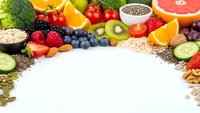 Colorful fresh fruits vegetables nuts seeds arranged in circle frame on white background. Healthy organic food ingredients for balanced nutrition diet.