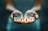 Open cupped hands reaching forward against dark background, glowing with warm light in palms, symbolizing hope, giving, spirituality and healing energy.