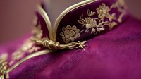 Elegant golden floral embroidery detail on rich purple velvet fabric, showcasing intricate needlework pattern with delicate flower motifs and metallic thread embellishments.