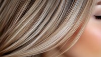 Close-up view of blonde highlighted hair strands flowing with soft focus effect showing natural shine and texture, suitable for beauty and hair care advertising.