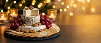 Gourmet cheese platter with crackers and grapes on wooden board, warm bokeh lights creating cozy atmosphere for holiday entertaining and festive gatherings.