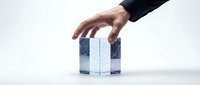 Hand of a middle-aged Caucasian male in business attire selecting or placing a translucent blue and white cube block, representing choice, decision-making, and corporate strategy.