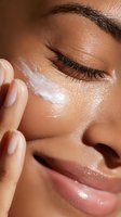 Close-up of African American woman applying moisturizer under eye, showcasing skincare routine with glowing complexion and manicured nails.