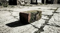 Old weathered brick lying on cracked concrete pavement with shadow, urban decay and abandoned construction materials concept.