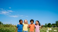 Young diverse children holding hands standing together in sunny meadow with clear blue sky, representing friendship, unity, and outdoor summer activities for families and educational content.