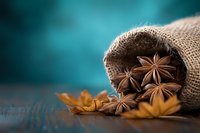 Star anise pods spilling from rustic burlap sack on dark wooden surface against turquoise background, creating aromatic cooking ingredients composition.