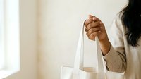 Woman with dark skin tone holding white reusable shopping bag, promoting sustainable lifestyle and eco-friendly consumer choices for retail and environmental campaigns.