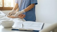 Healthcare professional performing therapeutic massage on patient's leg in modern medical clinic setting with natural lighting and treatment documentation.