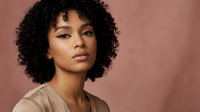 Young African American woman with curly hair and natural makeup against pink background for beauty and lifestyle content.