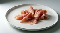Thin slices of cured ham arranged on white ceramic plate, premium deli meat for gourmet cooking and charcuterie boards in modern kitchen setting.
