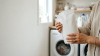 Mature woman holding clean white towel in laundry room with washing machine, domestic chore and household cleaning concept for home care and fabric care applications.