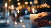 Glowing candle held in hand against blurred bokeh lights background creates atmospheric mood for spiritual, festive or memorial occasions.