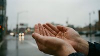 Open palm of a man catching raindrops during rainfall in urban setting with blurred city street and traffic lights in background. Suitable for weather, climate, nature, and environmental concepts.