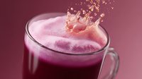 Fresh purple smoothie with dynamic splash crown effect in glass mug on burgundy background, frozen berry drink with dramatic lighting and motion capture.