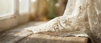 Delicate white lace fabric with intricate floral patterns draped on rustic wooden surface near bright window creating soft romantic atmosphere for textile design.