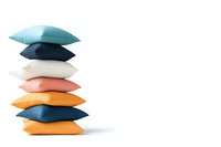 Stack of colorful decorative cushions in pastel and bright tones arranged vertically against white background, minimalist home decor composition.
