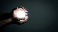 Male hands holding glowing orb of light against dark background, symbolizing innovation, ideas, energy, hope, and future potential for business and technology concepts.