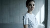 Young Caucasian female healthcare professional in white medical uniform standing confidently in modern hospital corridor with natural lighting.