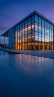 Modern glass office building illuminated at twilight with reflective water feature and dramatic purple sky for corporate architecture presentations.