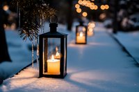 Cozy winter evening scene with glowing lanterns and candles in snow creating warm ambient lighting with bokeh lights and evergreen branches.