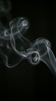Swirling white smoke curls and spirals against a deep black background, creating an abstract, ethereal flow of motion and texture.