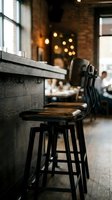 Modern bar stool with wooden seat at counter in industrial restaurant interior with warm ambient lighting and blurred diners in background.