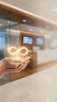 Hand holding glowing infinity symbol in modern office space, representing endless growth, sustainability, and continuous business potential for corporate concepts.